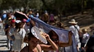 Туристы укрываются от солнца у входа на холм Акрополя во время жары в Афинах, в среду 9 июля 2025 года.