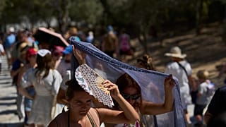Tourists take cover from the sun outside the entrance of the Acropolis hill during a heat wave in Athens, Wednesday, July 9, 2025. 