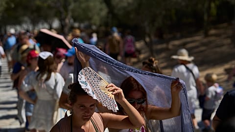 Tourists take cover from the sun outside the entrance of the Acropolis hill during a heat wave in Athens, Wednesday, July 9, 2025. 