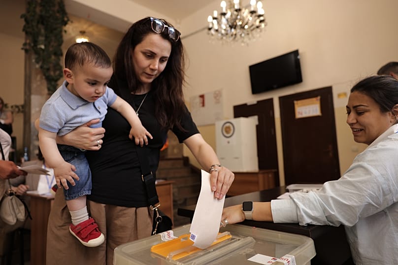 Une femme tenant un enfant dans ses bras dépose son bulletin de vote dans un bureau de vote lors d'une élection législative à Erevan, en Arménie