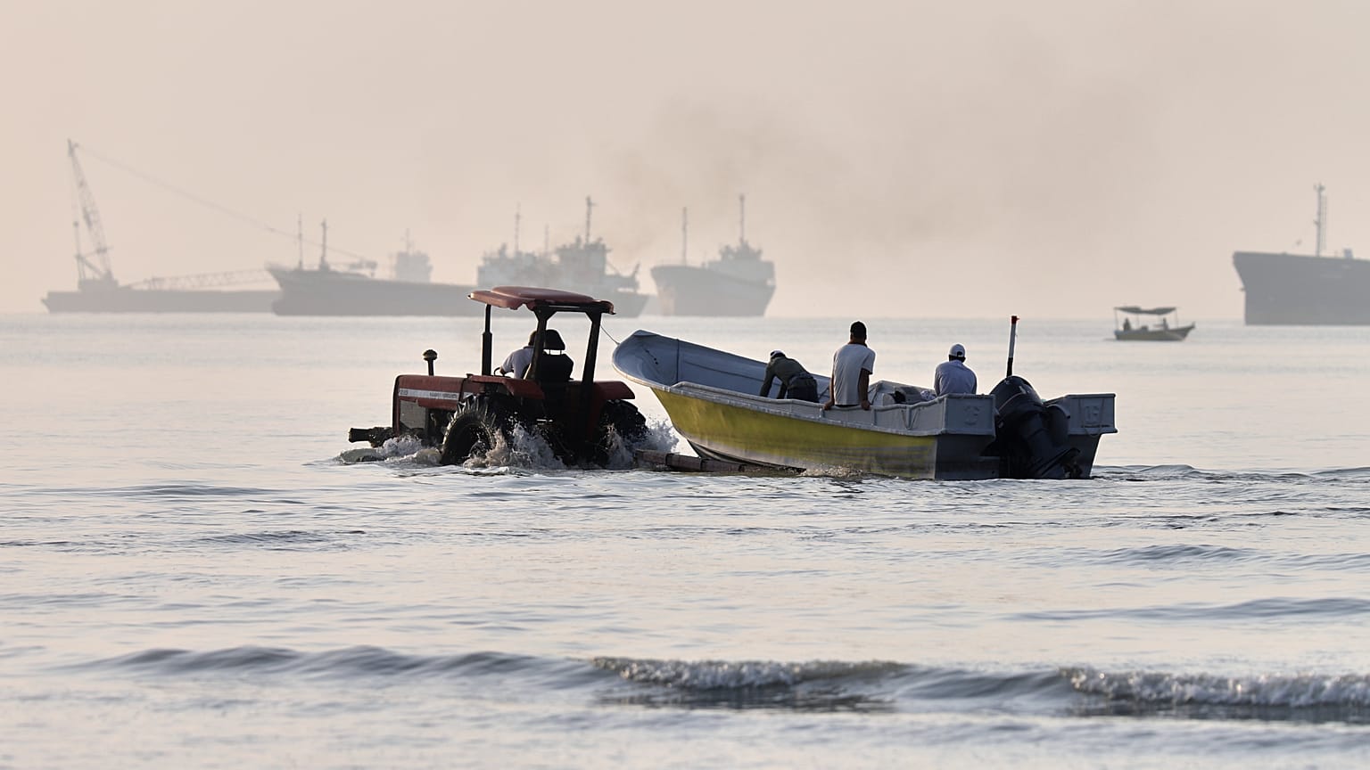 A tractor tows a small boat through shallow water as cargo ships and industrial vessels are anchored in the Strait of Hormuz off Bandar Abbas, Iran, Monday, June 1, 2026. 