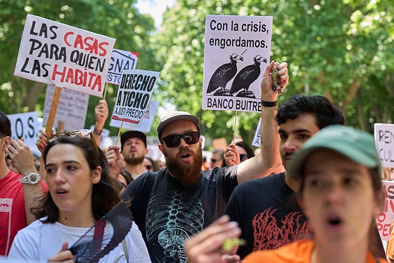 Több ember egy transzparenst tart, amelyen ez áll: "Lakás azoknak, akik benne élnek", egy 2026. május 24-i madridi tüntetésen, Spanyolországban.