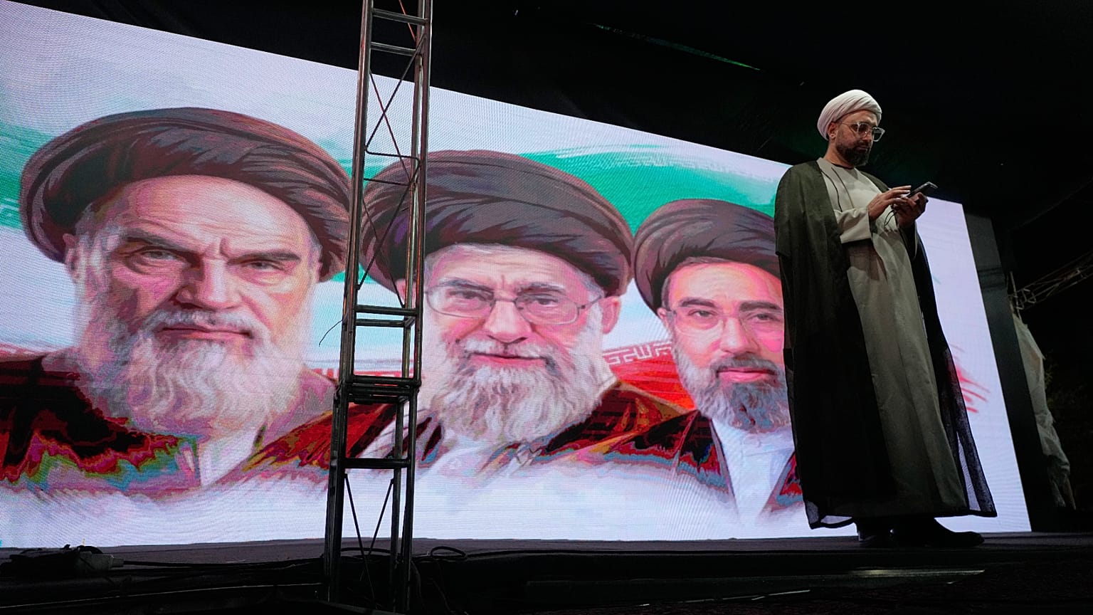 رجل دين يقف على منصة أمام صور آية الله روح الله الخميني وعلي خامنئي  ومجتبى خامنئي، طهران، 7 يونيو 2026.