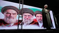 رجل دين يقف على منصة أمام صور آية الله روح الله الخميني وعلي خامنئي  ومجتبى خامنئي، طهران، 7 يونيو 2026.
