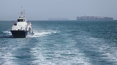 FILE: A patrol boat moves through the water as cargo ships sit at anchor in the Strait of Hormuz off Bandar Abbas, 2 May 2026