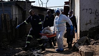 Agenti di polizia trasportano su una barella il corpo di una persona dopo una sparatoria di massa in un insediamento informale vicino a Johannesburg, 10 giugno 2026