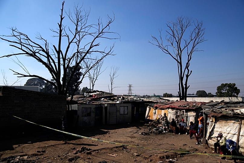 People sit outside a cordon at the scene of a mass shooting at an informal settlement near Johannesburg, 10 June, 2026