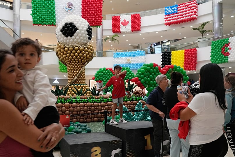 Clienti in piedi davanti alle bandiere gonfiabili dei Paesi partecipanti alle finali della Coppa del Mondo FIFA in un centro commerciale a Guadalajara, in Messico, martedì 9 giugno 2026. 