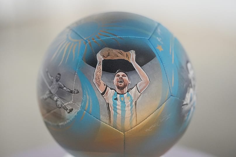 Az argentin Lionel Messi a világbajnoki trófeával egy futball-labdán, amelyet Lili Cantero művész kézzel festett, és amelyet Miamiban állítottak ki 2026. június 4-én