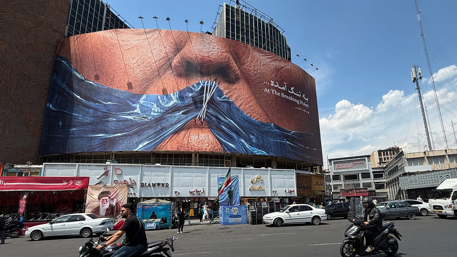 Vehicles drive past a billboard with graphic showing Strait of Hormuz and sewn lips of U.S. President Donald Trump in a square in downtown Tehran, Iran, Saturday, May 2, 2026.
