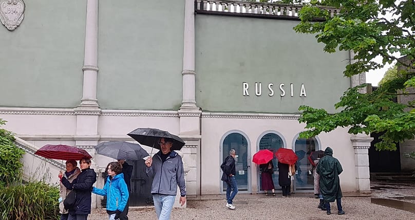 Закрытый 9 мая российский павильон на Венецианской биеннале. Посетители заглядывают в окна, через которые можно увидеть экспозицию "Дерево, укоренённое в небо", 14 мая 2026 г.