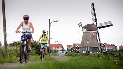 People bike past a windmill in Volendam, 19 July, 2014