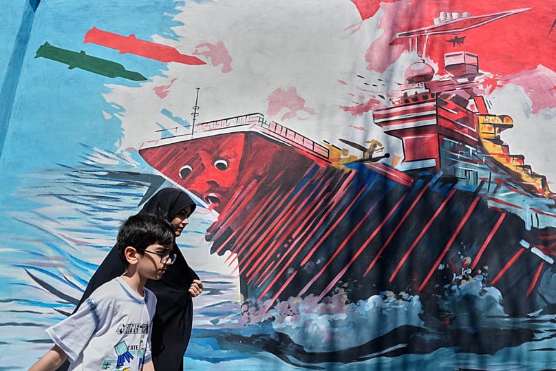 People walk past a mural depicting a US aircraft carrier under missile attack in downtown Tehran, 8 June, 2026