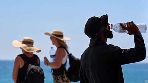 A tourist drinks from a bottle of water on the beach in Barcelona