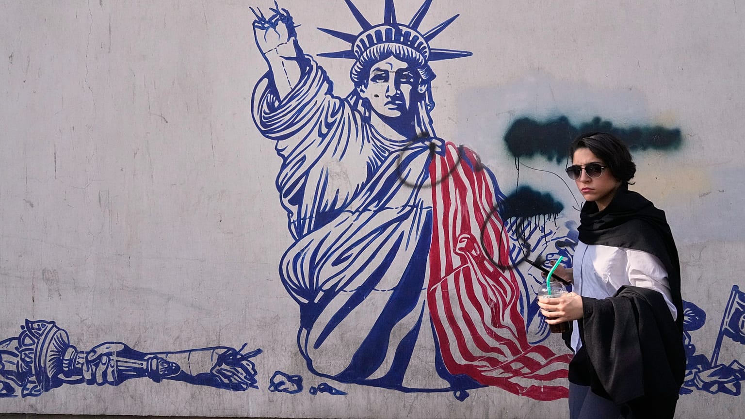 A woman walks past an anti-American mural on the wall of the former U.S. Embassy, now a museum, in Tehran, Iran, Friday, June 12, 2026. (AP Photo/Vahid Salemi)