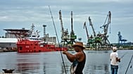 A fisherman prepares his fishing rod in front of the Colombian Navy ship ARC Caribe docked at a pier in Havana, 12 June, 2026