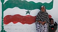  امرأة وطفل يسترخيان بجوار لوحة جدارية لعلم أرض الصومال، في هرجيسا، أرض الصومال
