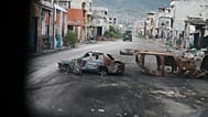 Burned cars block a street photographed from inside an armoured police vehicle patrolling a gang-controlled area in Port-au-Prince, 16 January, 2026