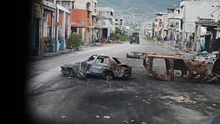 Verbrannte Autos blockieren eine Straße, gesehen aus einem gepanzerten Polizeifahrzeug in einem gangkontrollierten Viertel von Port-au-Prince, 16. Januar 2026.