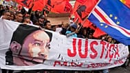 Um homem segura uma bandeira de Cabo Verde, enquanto outros carregam uma faixa com a imagem de Odair Moniz, um homem de origem cabo-verdiana que foi morto a tiro pela polícia