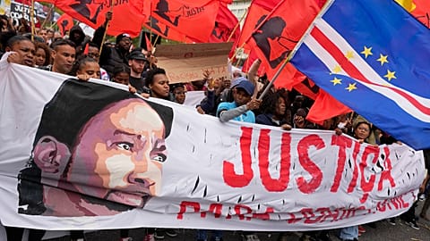 Um homem segura uma bandeira de Cabo Verde, enquanto outros carregam uma faixa com a imagem de Odair Moniz, um homem de origem cabo-verdiana que foi morto a tiro pela polícia