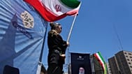 امرأة تلوّح بالعلم الإيراني خلال حملة مؤيدة للحكومة، بينما تُعرض صورة المرشد الأعلى الراحل آية الله علي خامنئي، الذي قُتل في غارات أمريكية وإسرائيلية في 28 فبراير، على اليمين،