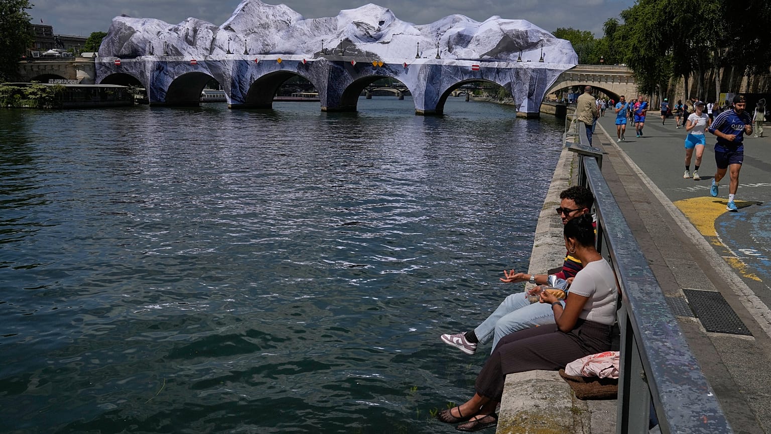 Menschen sitzen an der Seine neben „The Pont Neuf Cave“, einer aufblasbaren Kunstinstallation des französischen Street-Art-Künstlers JR.