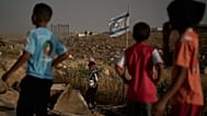 طفل فلسطيني يستعيد كرة قدم بعد أن سقطت خلف سياج من الأسلاك الشائكة أقامه مستوطنون إسرائيليون بجوار ملعب كرة قدم في قرية أم الخير البدوية بالضفة الغربية، الثلاثاء 12 مايو/أيار 