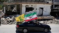 يحمل نازحون علمًا إيرانيًا وآخر لحزب الله أثناء مرورهم بجانب مبنى مدمّر تعرّض لغارة جوية إسرائيلية سابقة في بلدة الشهابية جنوب لبنان، الثلاثاء 16 يونيو/حزيران 2026.