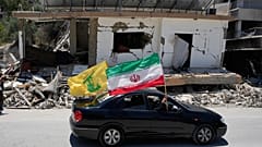 يحمل نازحون علمًا إيرانيًا وآخر لحزب الله أثناء مرورهم بجانب مبنى مدمّر تعرّض لغارة جوية إسرائيلية سابقة في بلدة الشهابية جنوب لبنان، الثلاثاء 16 يونيو/حزيران 2026.
