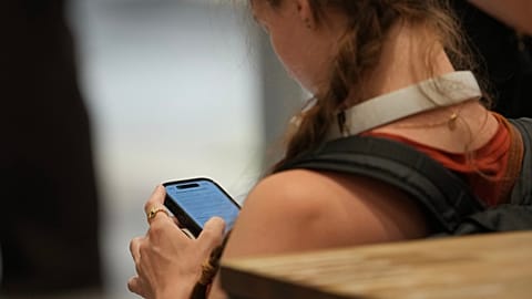 FILE - A teenager looks at her mobile phone in London, 15 June 2026. (AP Photo/Kin Cheung)
