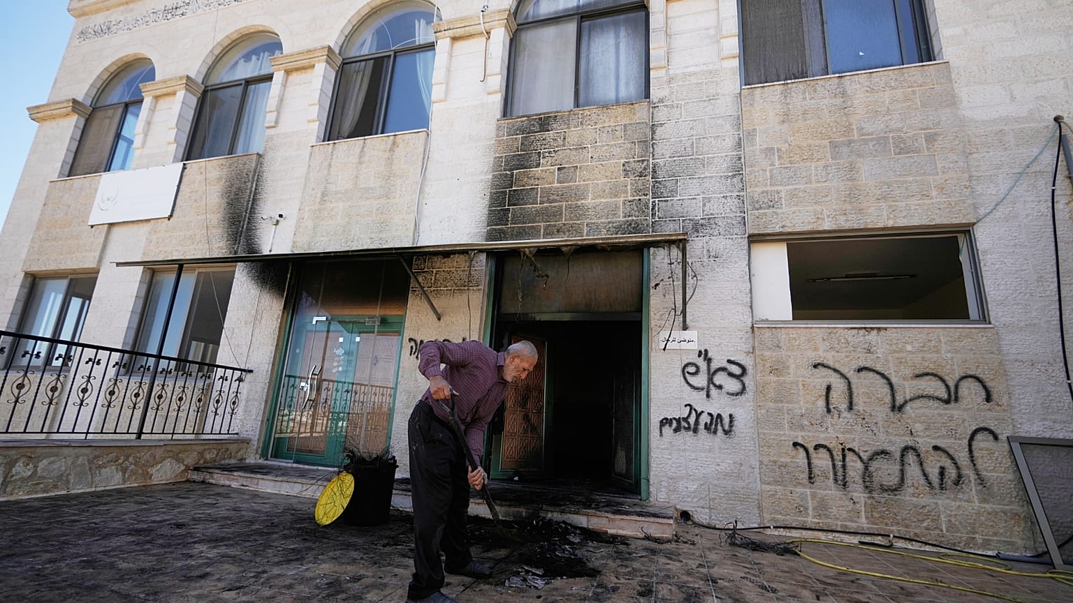 A man removes rubble from a West Bank mosque damaged in an overnight attack, with Hebrew graffiti calling for "revenge" scrawled on a wall.