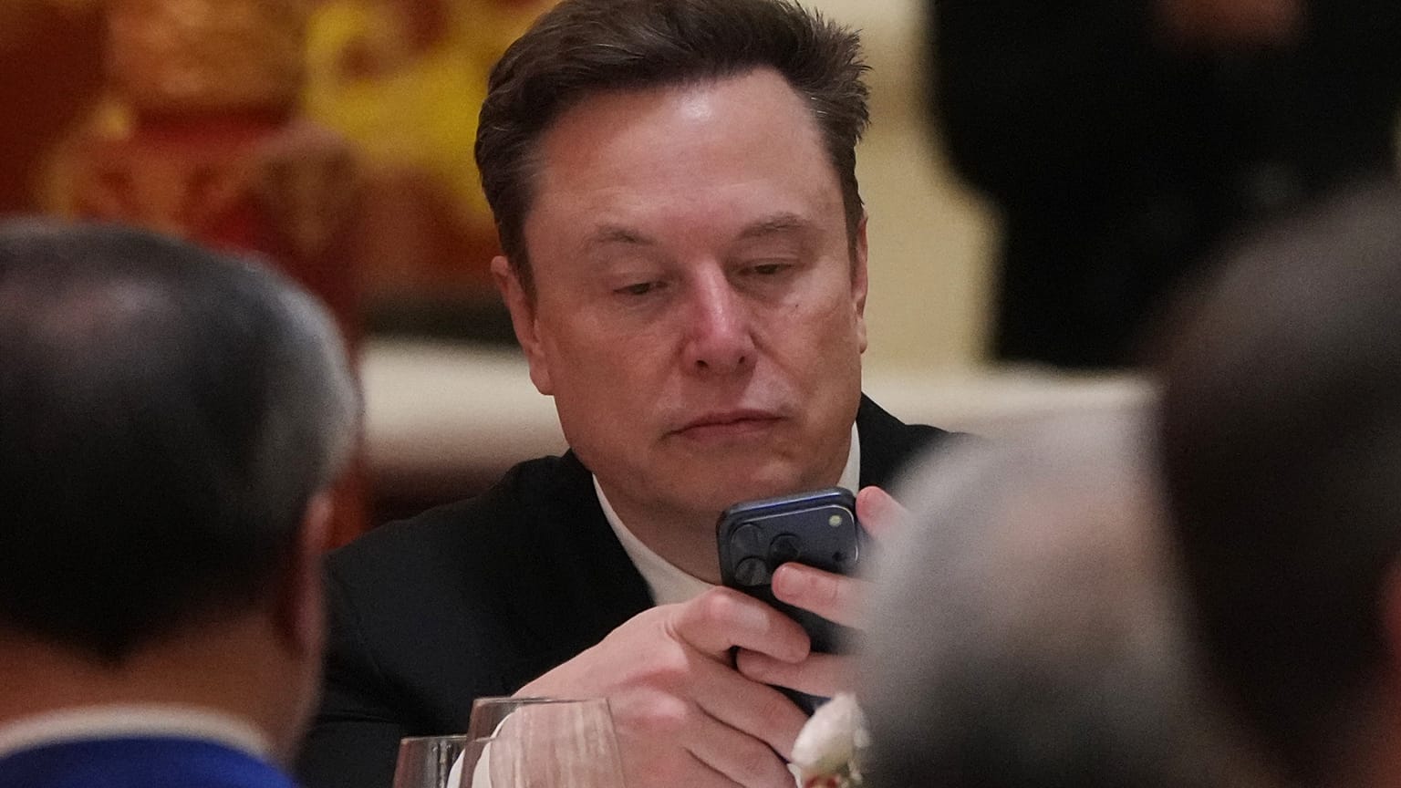 Elon Musk uses his phone during a state dinner for President Donald Trump and Chinese President Xi Jinping at the Great Hall of the People on Thursday May 14, 2026, in Beijing