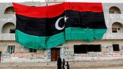 مواطنون ليبيون يمرون بمبنى يحمل العلم الليبي القديم الضخم، في بنغازي، شرق ليبيا، الجمعة 4 مارس 2011.