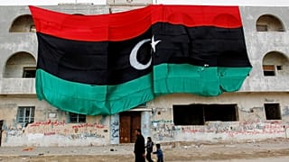 مواطنون ليبيون يمرون بمبنى يحمل العلم الليبي القديم الضخم، في بنغازي، شرق ليبيا، الجمعة 4 مارس 2011.