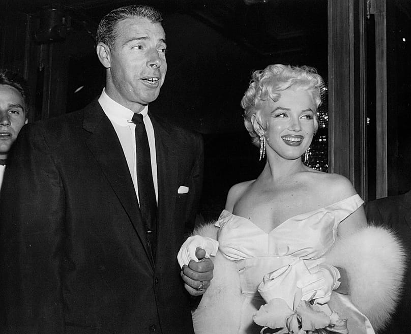 Ezen az 1955. június 2-i archív fotón Marilyn Monroe színésznő (jobbra), aki elbűvölő estélyi ruhát visel, Joe DiMaggióval együtt érkezik a színházba.