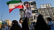 امرأة ترفع العلم الإيراني أمام لافتة تحمل صورة المرشد الأعلى آية الله مجتبى خامنئي خلال مهرجان شعبي احتفالاً بعيد الغدير، ذكرى تسمية النبي محمد صلى الله عليه وسلم لخليفته علي 