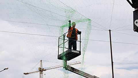 Egy önkormányzati dolgozó drónelhárító hálót szerel fel, hogy megelőzze az emberek és a közlekedés elleni orosz támadásokat Zaporizzsjában, Ukrajnában, 2026. június 18-án.