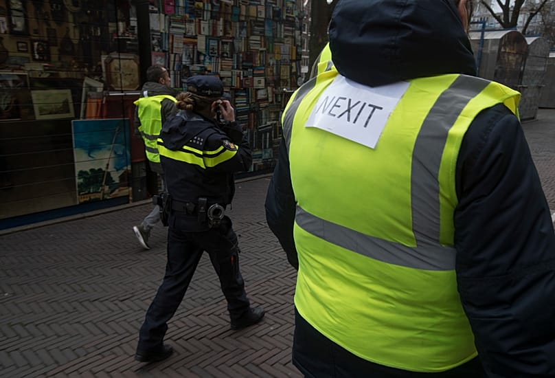 A demonstrator carries a NEXIT sign on his yellow vest as a Dutch Police officer walks alongside a peaceful demonstration in Amsterdam, Netherlands, Saturday, Dec. 8, 2018. 