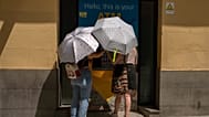 Two woman at an ATM protect themselves from the sun with umbrellas during a heatwave in Madrid, Spain, Sunday, Aug. 15, 2021.