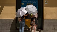 Zwei Frauen schützen sich an einem Geldautomaten in Madrid mit Regenschirmen vor der Sonne. In Spanien herrscht am Sonntag, 15. August 2021, eine Hitzewelle.