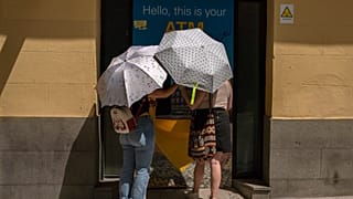 Madrid : deux femmes se protègent du soleil avec des parapluies devant un distributeur automatique lors d'une vague de chaleur, le dimanche 15 août 2021.