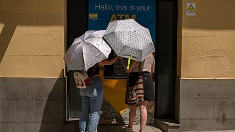 Two woman at an ATM protect themselves from the sun with umbrellas during a heatwave in Madrid, Spain, Sunday, Aug. 15, 2021.