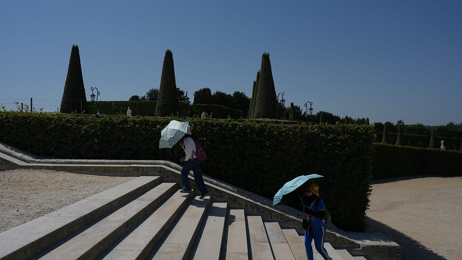 Besucher schützen sich mit Regenschirmen vor der Sonne und spazieren durch die Gärten von Schloss Versailles – mitten in einer Hitzewelle.