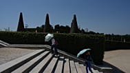 Visitors shield themself from the sun with umbrellas as they walk in the garden of the Palace of Versailles, during a heat wave. 