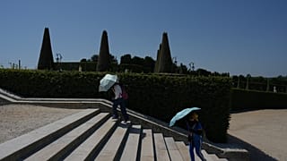 Visitors shield themself from the sun with umbrellas as they walk in the garden of the Palace of Versailles, during a heat wave. 