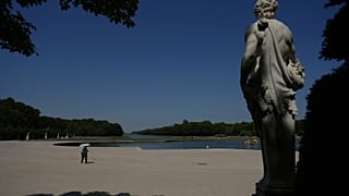 Kobieta osłania się przed słońcem parasolką, spacerując po ogrodach Wersalu podczas fali upałów z temperaturą przekraczającą 40°C.