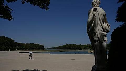 A woman shields herself from the sun with an umbrella as she walks in the garden of the Palace of Versailles during a heat wave with temperatures soaring above 40 °C.