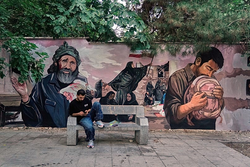 Ein Mann mit Smartphone vor einem Wandbild in Nord-Teheran, das Kinder ehrt, die bei einem Angriff in der südlichen Stadt Minab mutmaßlich durch einen US-Luftschlag getötet wurden, 15. Juni 2026