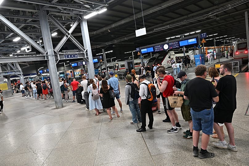 Passengers stand in line at the DB information desk at the Munich train station, Tuesday, June 23, 2026